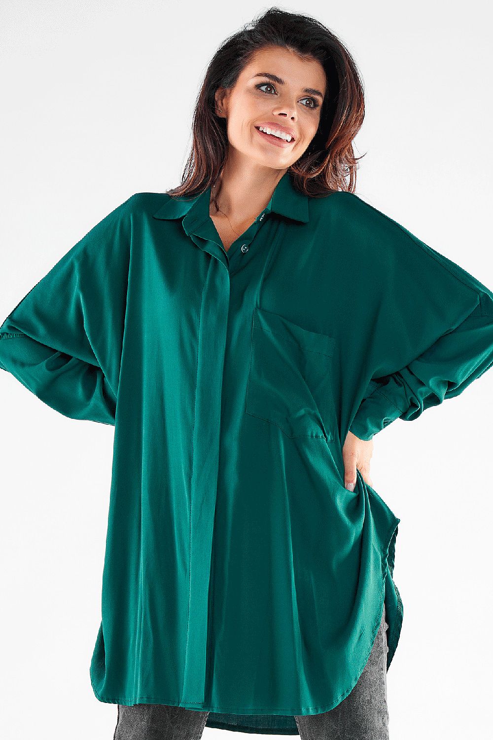 Chic women's oversized shirt in rich green, featuring a relaxed cut and a front pocket, perfectly paired with stylish grey denim for a sophisticated look.
