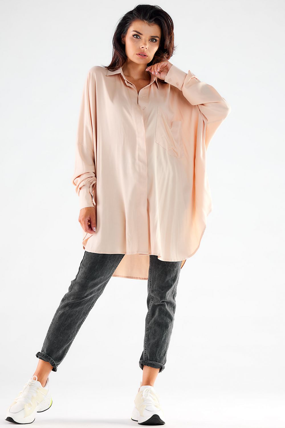 Front view of a sophisticated blush pink oversized long sleeve shirt on a woman, paired with grey jeans and white sneakers, ideal for chic casual styling.