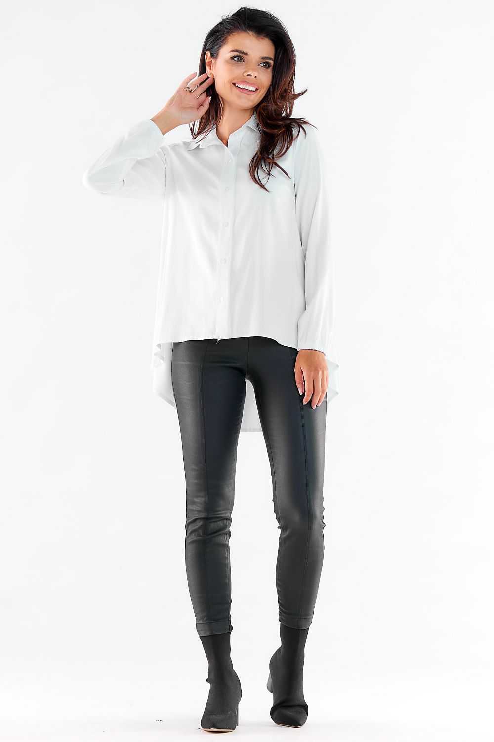 Chic long sleeve white shirt featuring an extended back, paired with sleek imitation leather pants, presented in an urban fashion context.