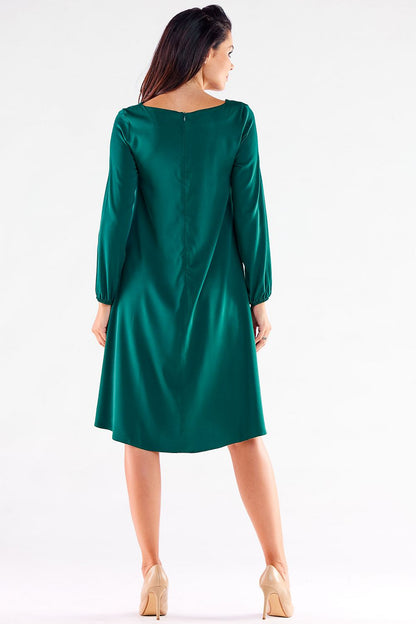 Elegant woman's trapezoidal daydress in deep green, featuring long sleeves and a gently extended back, ideal for versatile styling, showcased from the back.
