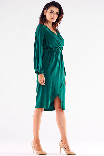 Sophisticated side profile of a model wearing a green long-sleeved Awama cocktail dress with a V neckline and a graceful slit, exuding luxury and elegance.