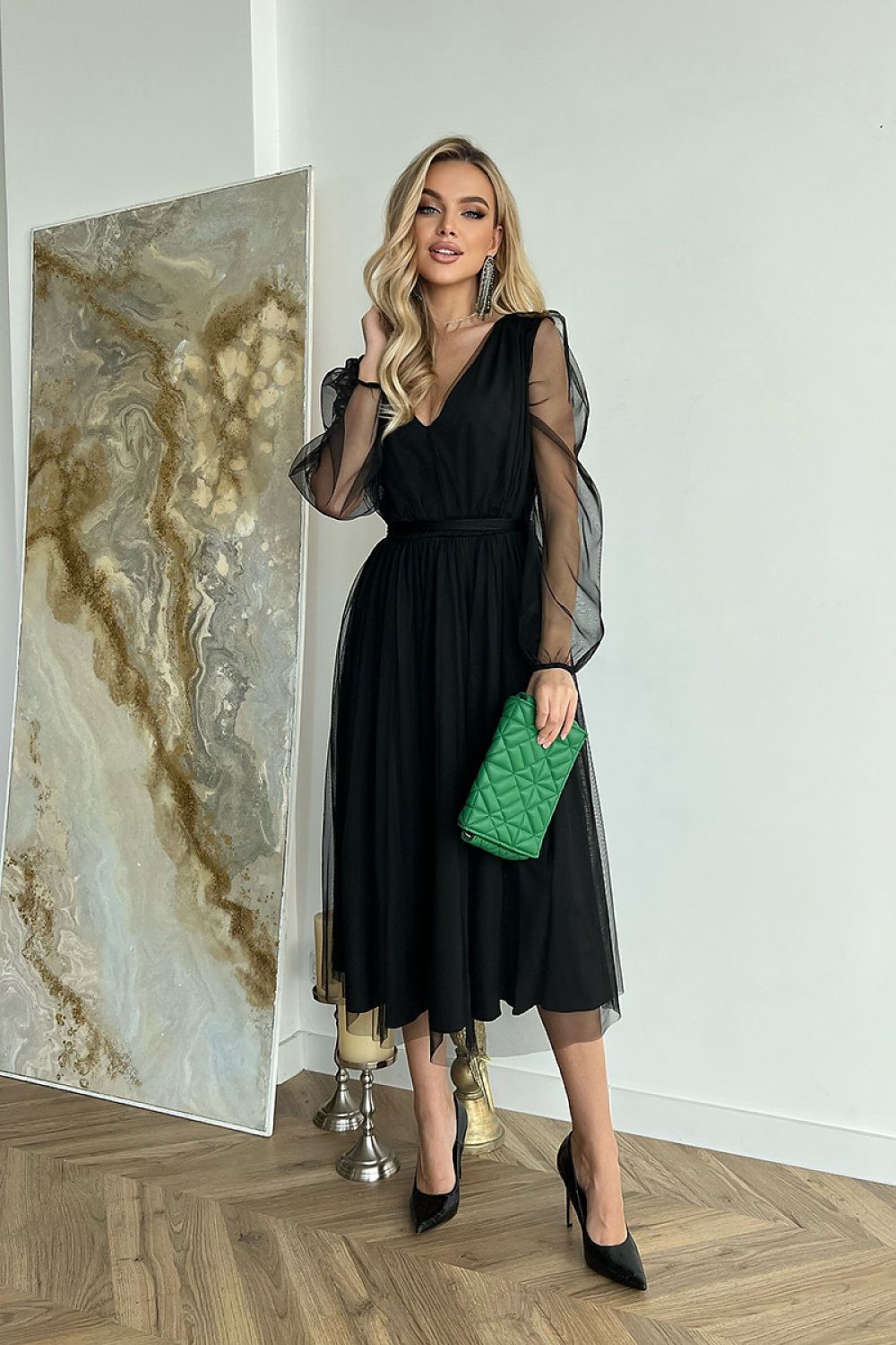 Striking black midi dress with transparent long sleeves, elegantly styled with a deep v-neck, paired with a green handbag, conveying timeless sophistication.