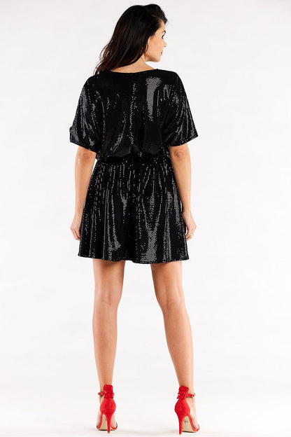 Back view of a sophisticated black flared evening dress featuring a sweetheart neckline and short sleeves, complemented by an elastic waistband, displayed on a model in red heels.