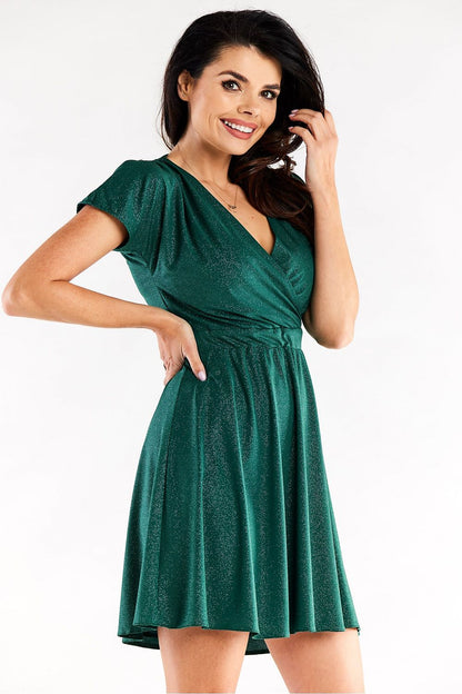 Glamorous model displaying an elegant short flared evening dress in deep green by Awama, featuring a flattering wrap design and elastic waist for comfort.