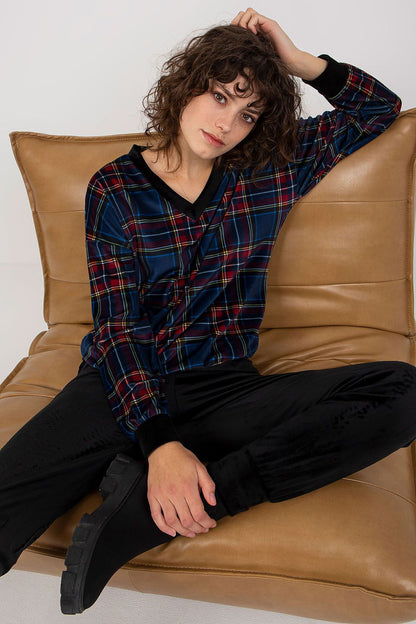 Stylish model in a navy checkered velour blouse and black pants, seated gracefully on a plush chair, epitomizing casual luxury and sophistication.