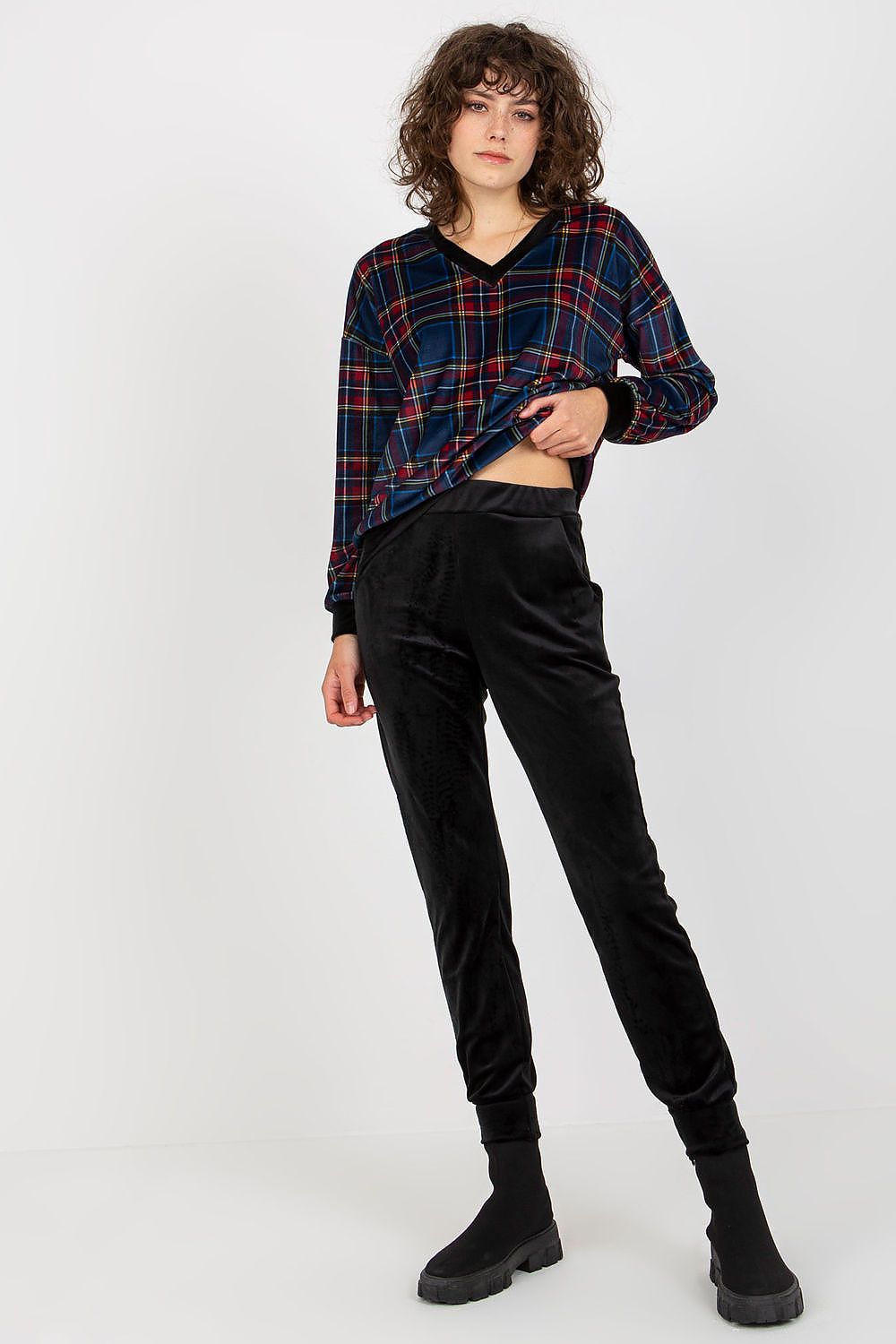 Confident pose of a model in a navy checkered blouse and sleek black velour trousers, exuding elegance and modern fashion vibes.