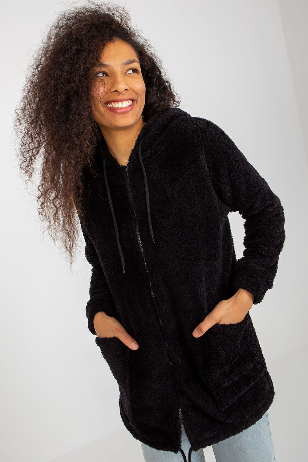 Luxurious black fur zip-up sweatshirt with hood, featuring large slip pockets, modelled by a woman with curly hair, exuding elegance and warmth.