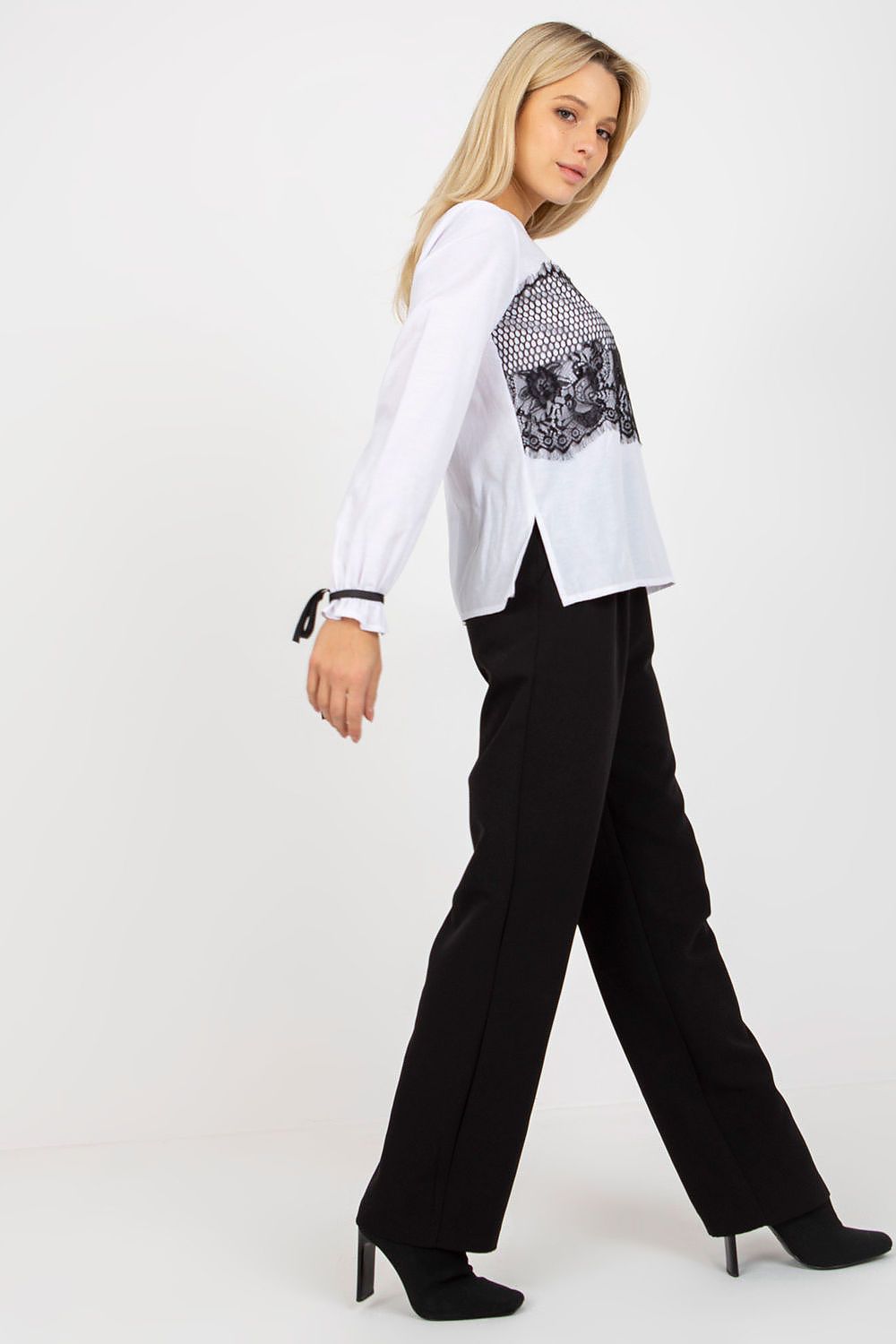 Chic side view of a beautiful model showcasing a white luxury cotton blouse adorned with decorative lace, styled with tailored black trousers.