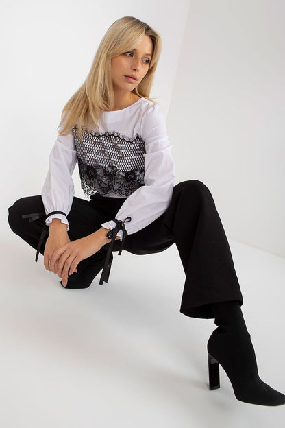 Fashionable pose of a model wearing a luxury white cotton blouse with intricate lace and stylish sleeves, complemented by tailored trousers.