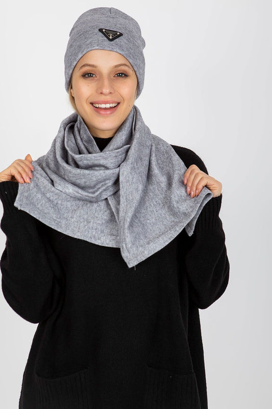 Elegant winter fashion featuring a model wearing a luxurious Angora and spandex hat and scarf set in soft grey. The model smiles warmly while showcasing the stylish scarf draped around her neck.