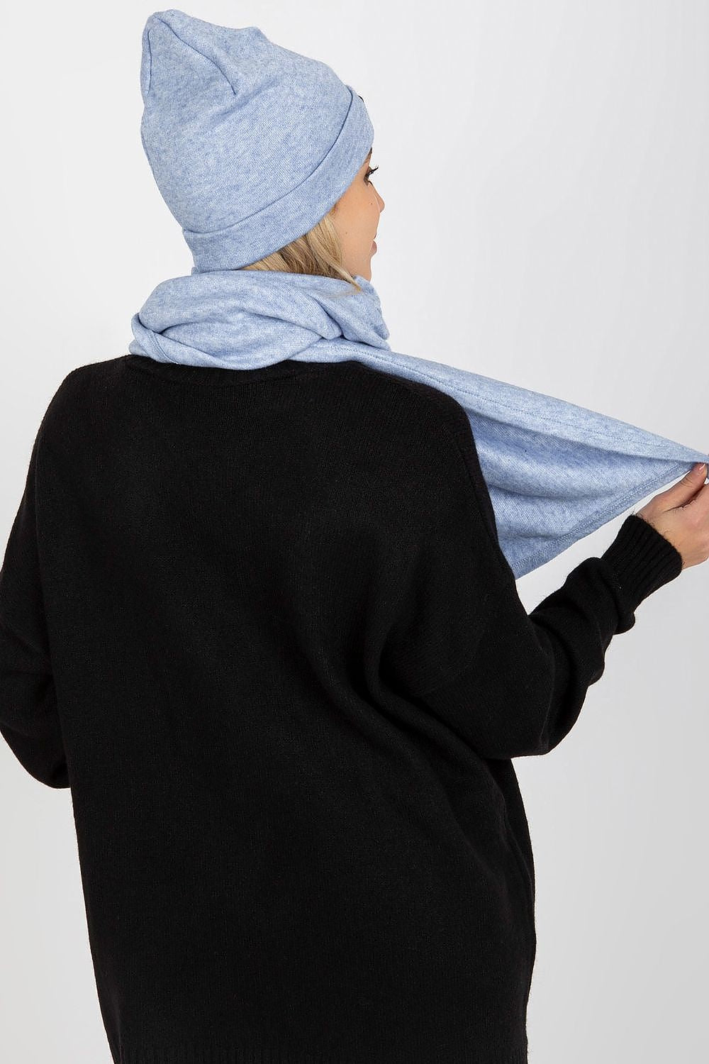 Elegant woman showcasing a luxurious Lakerta Angora and Spandex winter set, featuring a soft blue hat and scarf, styled with a black oversized sweater against a minimalist backdrop.
