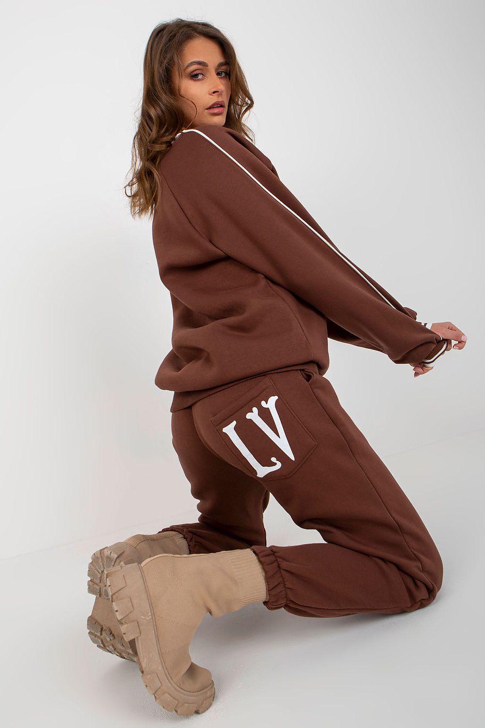 Fashionable brown sweatshirt set with a stylish logo, complemented by matching pants and elegant beige boots, exuding sophistication in a modern, minimalist setting.