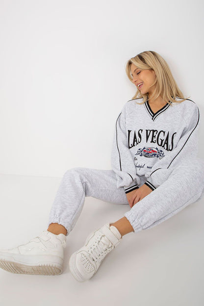 Elegant model in a grey sweatshirt set adorned with iconic graphics, perched stylishly on the floor, accentuated by fashionable white sneakers imbued with luxury.