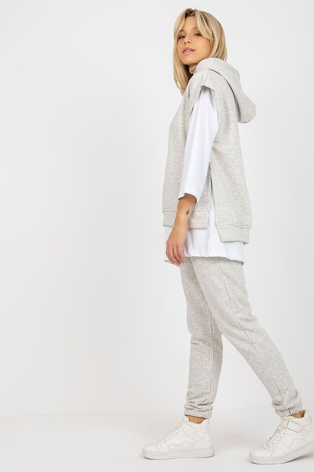Trendy light grey 3-piece sweatsuit featuring a stylish sleeveless hoodie with side slits, paired with elegant sneakers, designed for effortless, fashionable comfort.