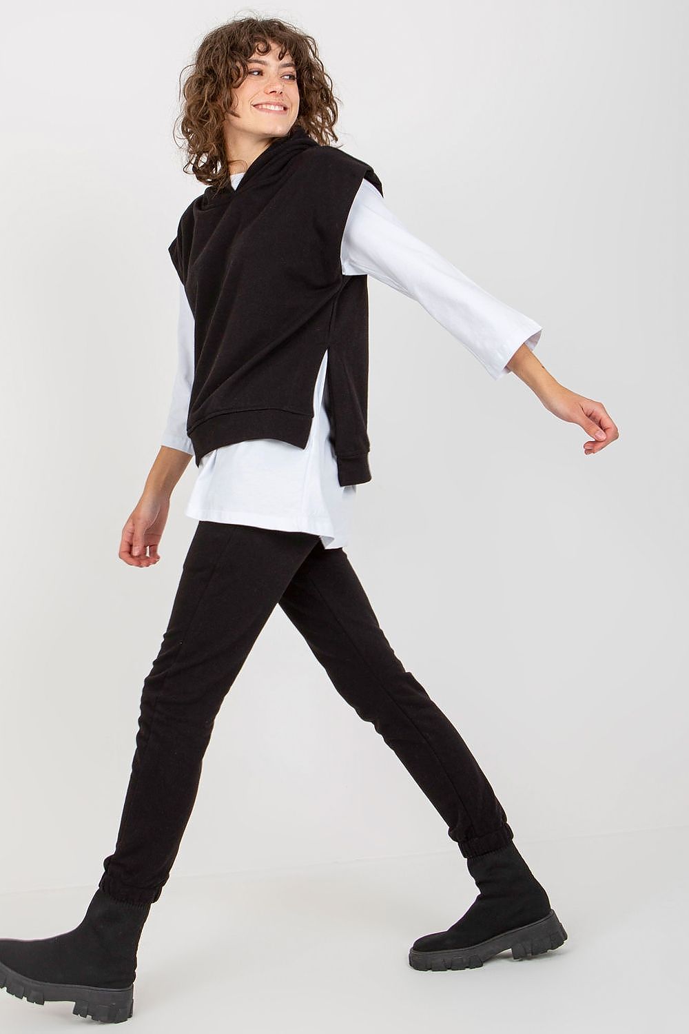 Elegant model showcasing a premium black 3-piece sweatsuit set with a stylish sleeveless hoodie, layered over a long-sleeve blouse, paired with tailored black pants, perfect for chic casual wear.