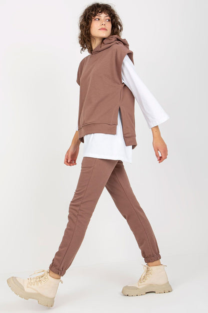 Stylish model showcasing a fashionable brown sweatsuit set, with a sleeveless hoodie over a white blouse, paired with tailored pants, exuding a sense of modern elegance.
