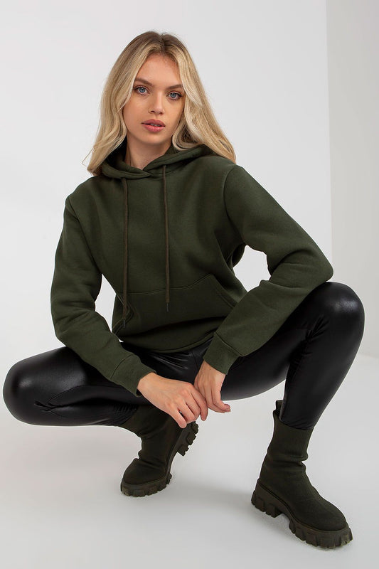 Luxury women's hooded sweatshirt by Rue Paris in deep green, featuring a kangaroo pocket. The model showcases the comfortable fit paired with sleek black leggings and stylish ankle boots, embodying casual elegance.