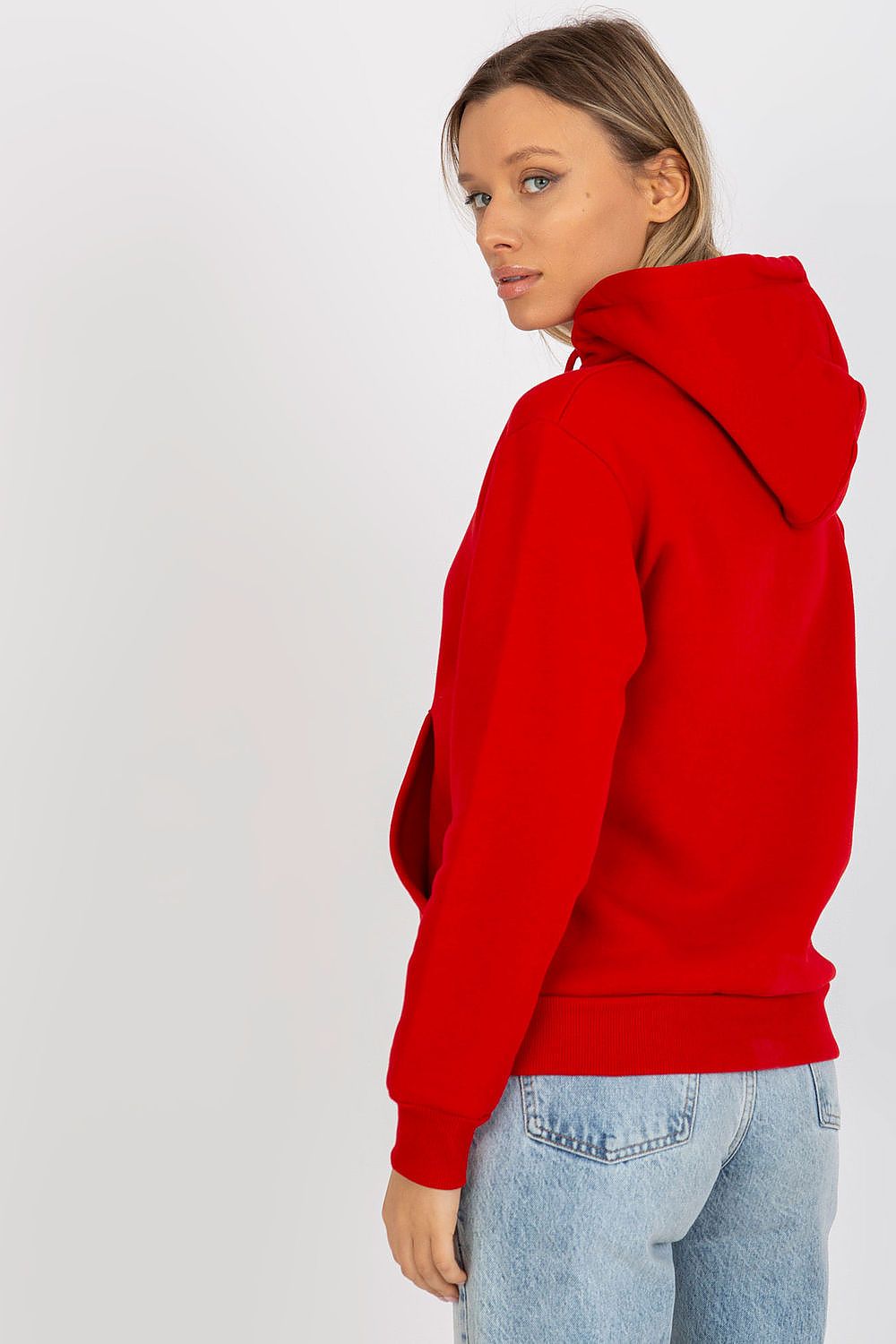 Elegant woman showcasing a red hooded sweatshirt from Rue Paris, featuring a kangaroo pocket, paired with trendy light denim jeans, embodying luxury casual style.