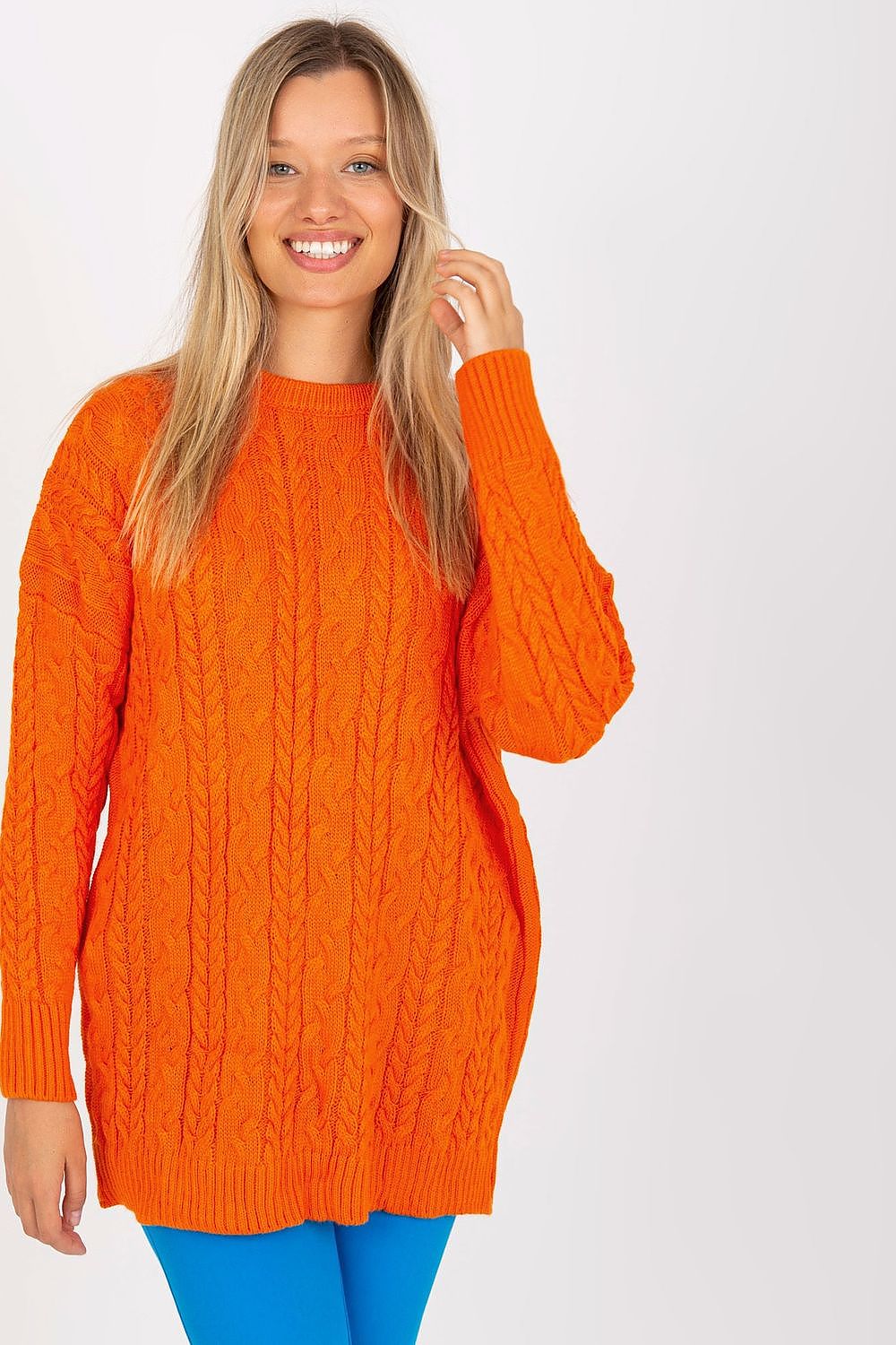 Smiling model in a vibrant orange long-sleeved knit sweater by Rue Paris, characterized by a luxurious chunky knit design, complementing blue leggings for a trendy outfit.