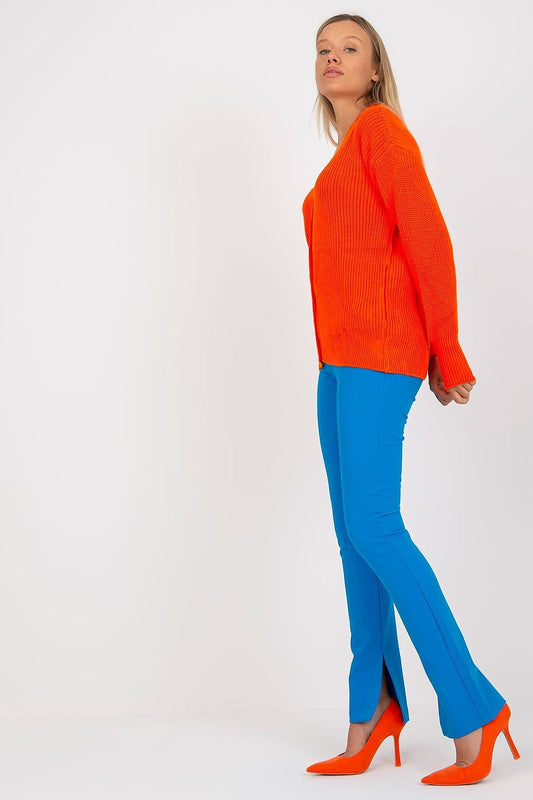 Side view of a stylish Rue Paris Women's acrylic cardigan in bright orange, complemented by blue trousers and high-heeled shoes, highlighting modern fashion trends.