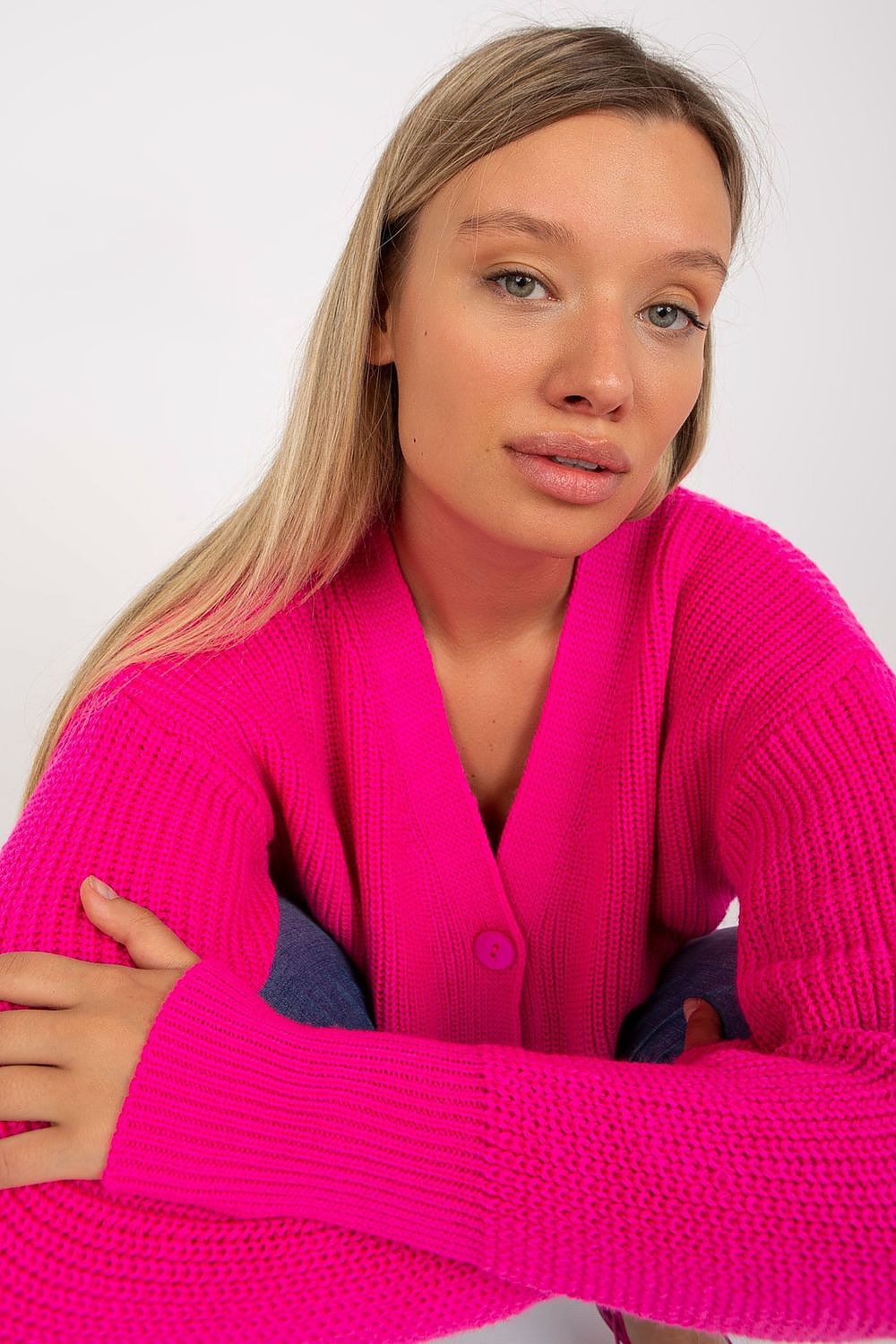 A close-up of a woman wearing an elegant vibrant pink long-sleeve cardigan with a button closure, showcasing a casual yet sophisticated style.