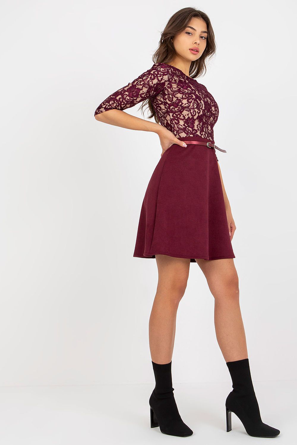 Side view of an elegant burgundy evening dress featuring a stunning lace top, 3/4 sleeves, and a lined skirt, complemented by a stylish buckled belt. The model is wearing fashionable ankle boots, showcasing a sophisticated look perfect for formal occasions.