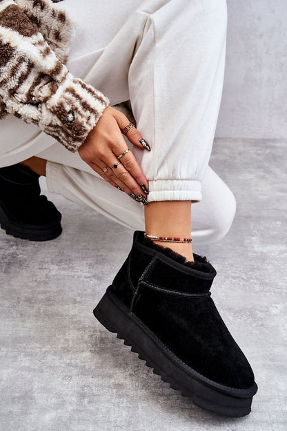 Close-up of luxury black snow boots with a plush eco-friendly fur lining, modelled with white sweatpants and trendy jewellery.