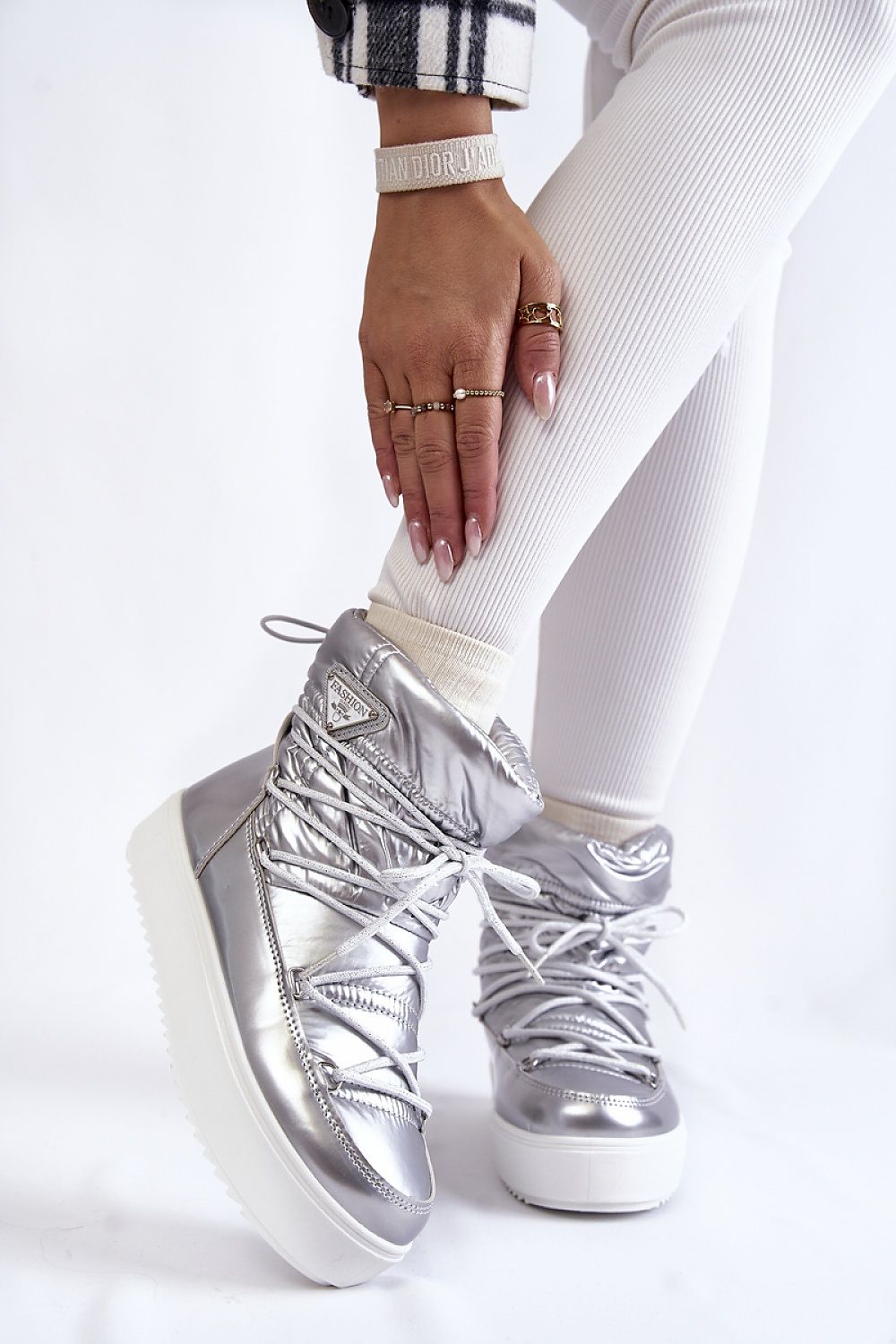 Glamorous women's snow boots in shiny silver finish, enriched with warm insulation, highlighted on a model dressed in contemporary winter attire.