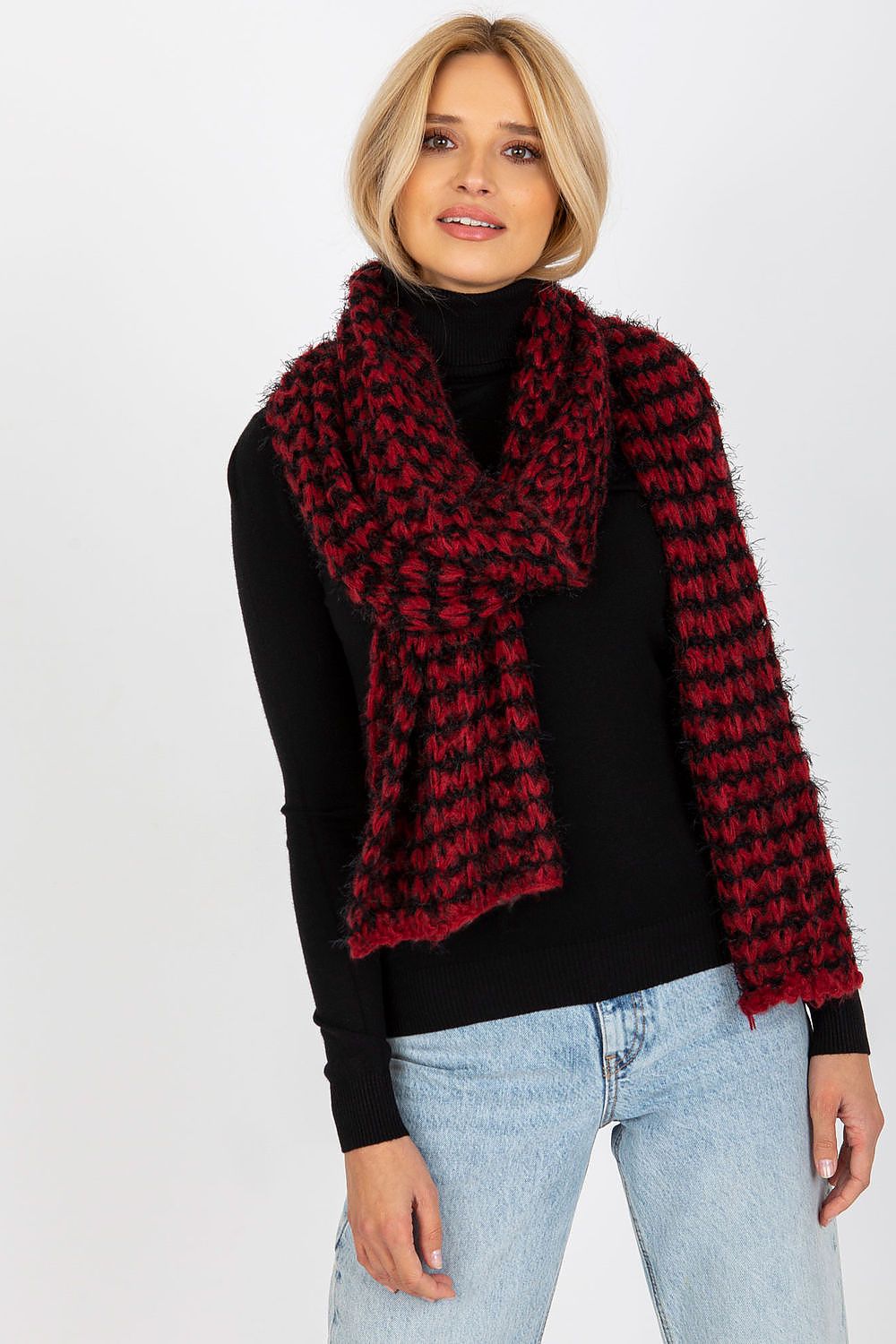 Elegant female model wearing a luxurious knitted acrylic shawl scarf in black and red, styled with a fitted black turtleneck and light jeans, showcasing warmth and sophistication.