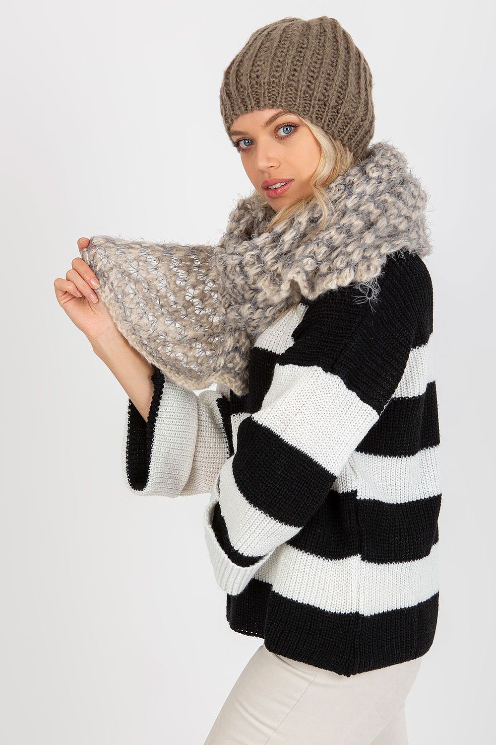 Stylish model in a black and white striped sweater holding a luxurious beige and grey knitted scarf, exemplifying cosy elegance.