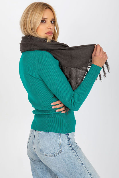 Chic woman wearing a sophisticated dark tasselled shawl scarf, elegantly draped over a teal sweater, illustrating modern luxury.