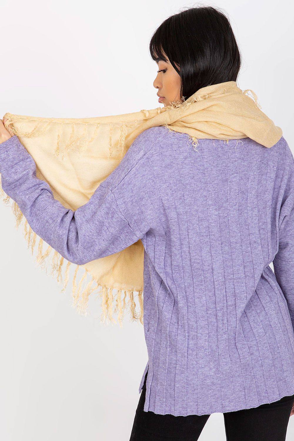 Elegant view of a woman wearing a golden shawl scarf with tassels around her shoulders, highlighting fashion versatility and comfort.