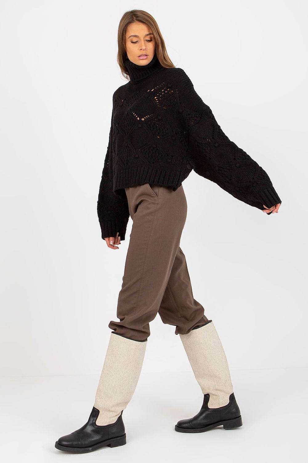 Side view of a luxurious black openwork turtleneck sweater with wide sleeves, paired with brown trousers and chic knee-high boots.