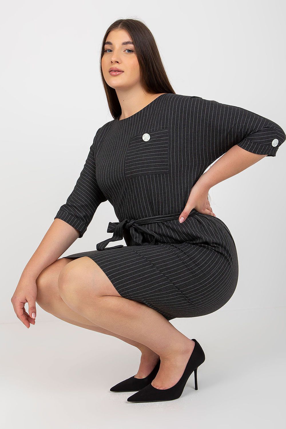 Chic plus size pencil dress in black and white striped fabric, model demonstrating a trendy squat pose, complemented by elegant heels.