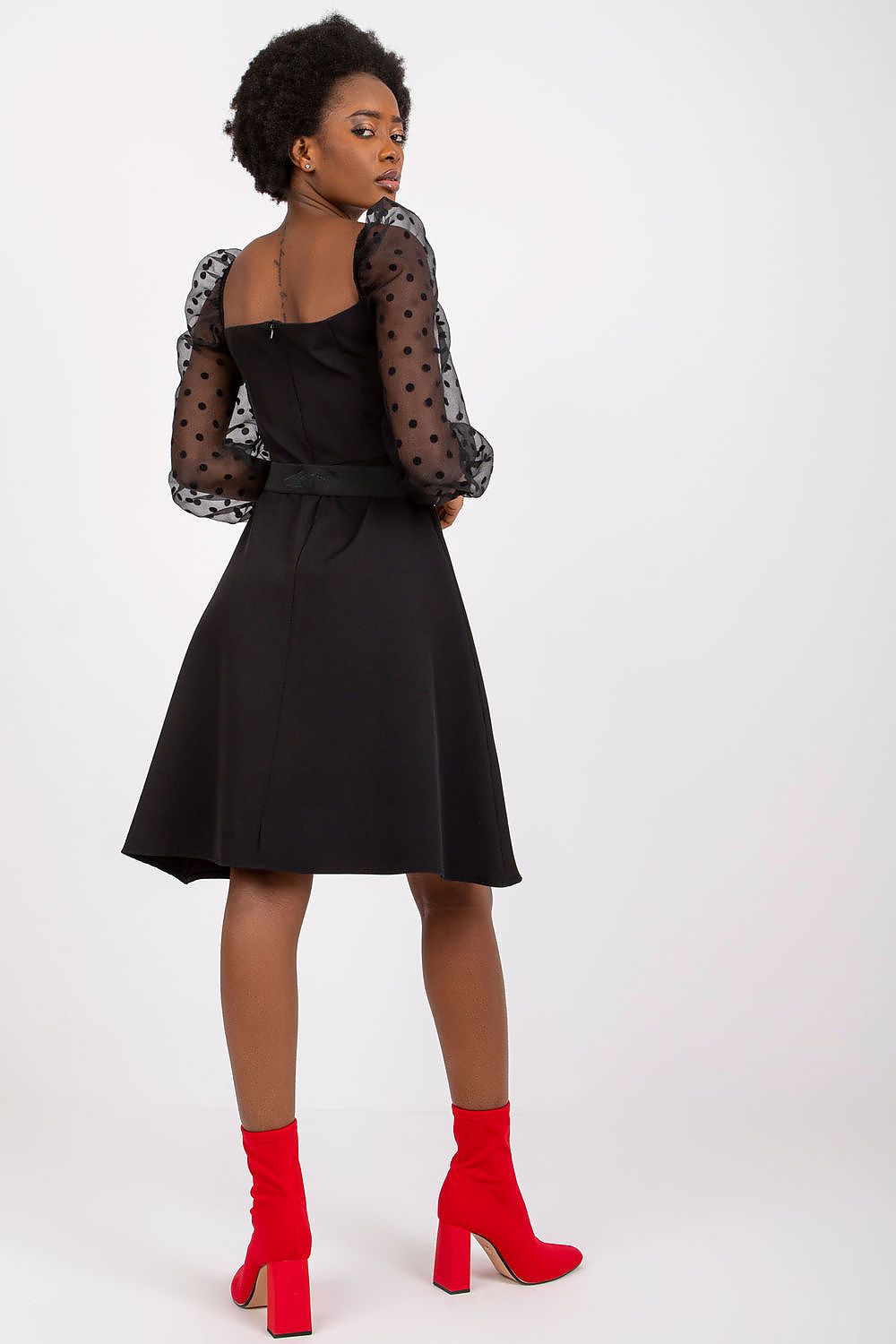 Elegant black evening dress with 3/4 polka dot sleeves and a flattering silhouette, accented by a stylish belt and a covered zipper closure, showcased on a model wearing fashionable red ankle boots.