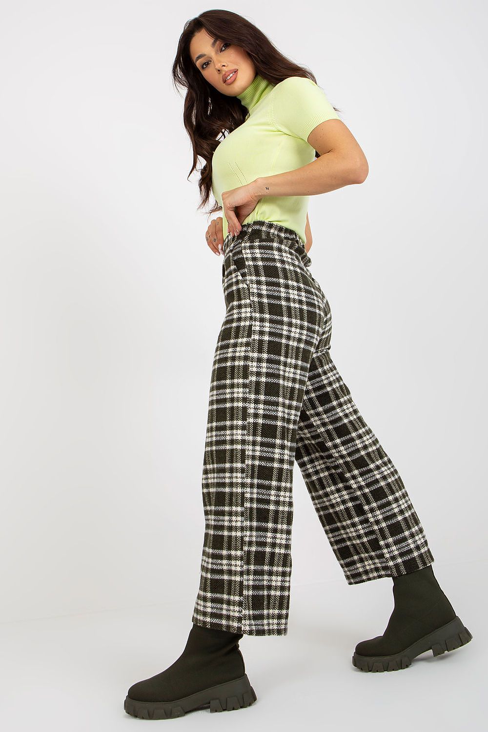Stylish woman in a lime green turtleneck and checkered wool trousers, posing gracefully to emphasise a fashionable ensemble.