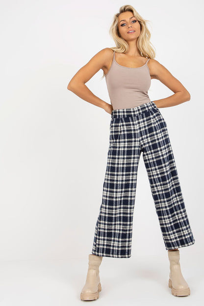Stylish model exuding luxury in checkered wool trousers, complemented by a chic beige tank top, posing confidently with hands on hips.