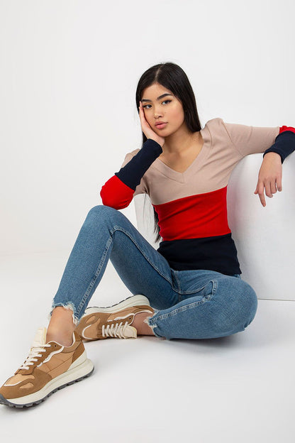 Chic model seated gracefully in a luxurious ribbed blouse with long sleeves and heart neckline, featuring a trendy colour block pattern, paired with denim, exuding contemporary elegance.