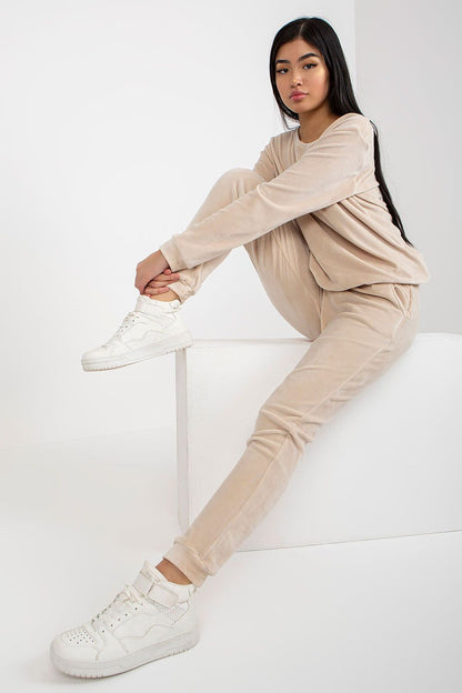 Elegant model showcasing a luxurious velour blouse and pants set by Rue Paris, styled in a soft beige tone, featuring a relaxed fit and paired with chic white sneakers against a minimalistic background.