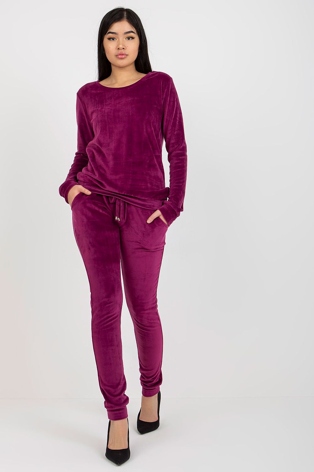 Chic model in a rich purple velour blouse and pants set, featuring long sleeves and a stylish tied waist, complemented with elegant high heels for a luxurious appeal.