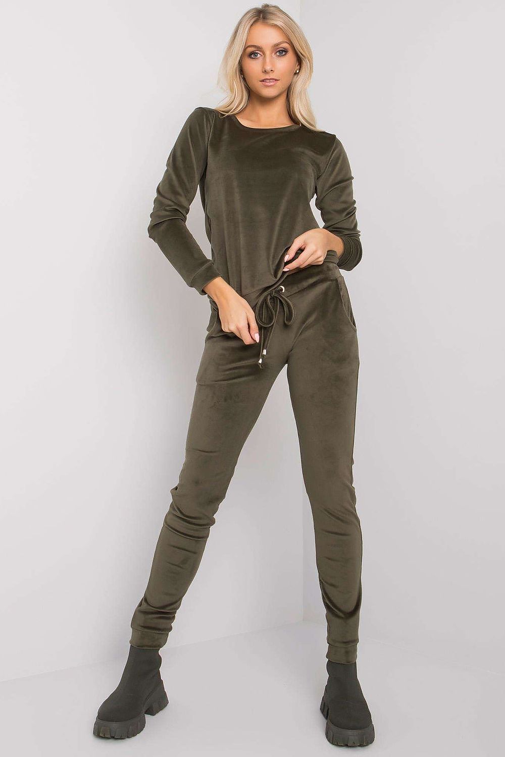 Elegant model presenting an olive green velour blouse and pants set by Rue Paris, designed with a tie waist and slip pockets.