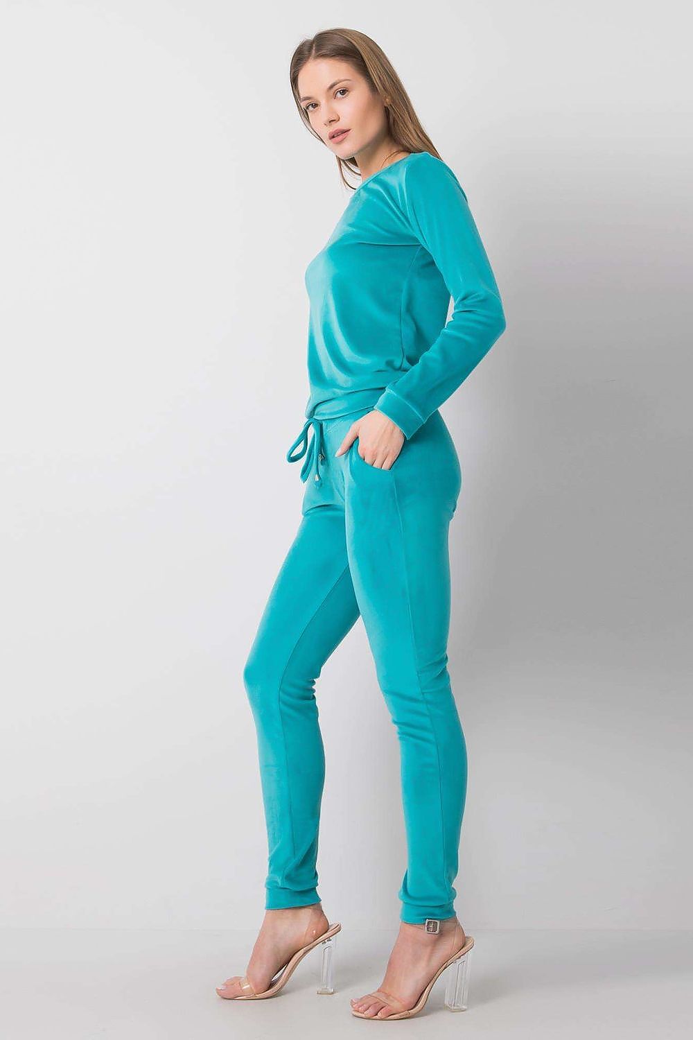 Chic woman in a turquoise velour blouse and pants ensemble with a tie waist and elegant silhouette, demonstrating a relaxed yet refined aesthetic.