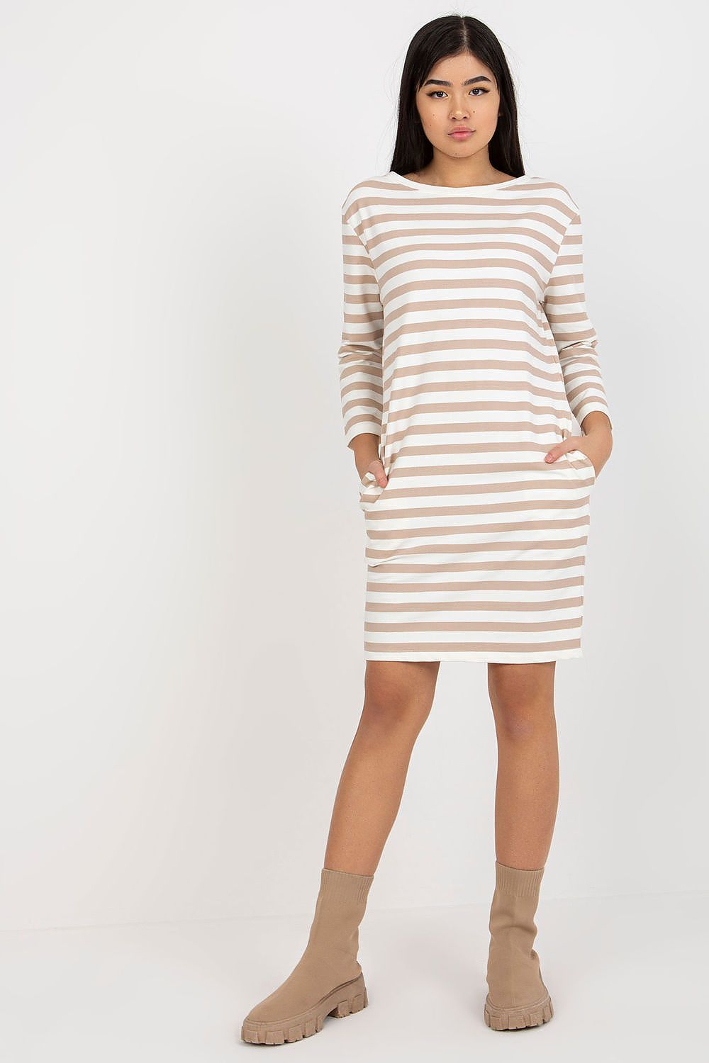 Elegant striped cotton dress with long sleeves, featuring side pockets, modelled standing with a minimalist backdrop. Perfect for chic casual wear by Rue Paris.
