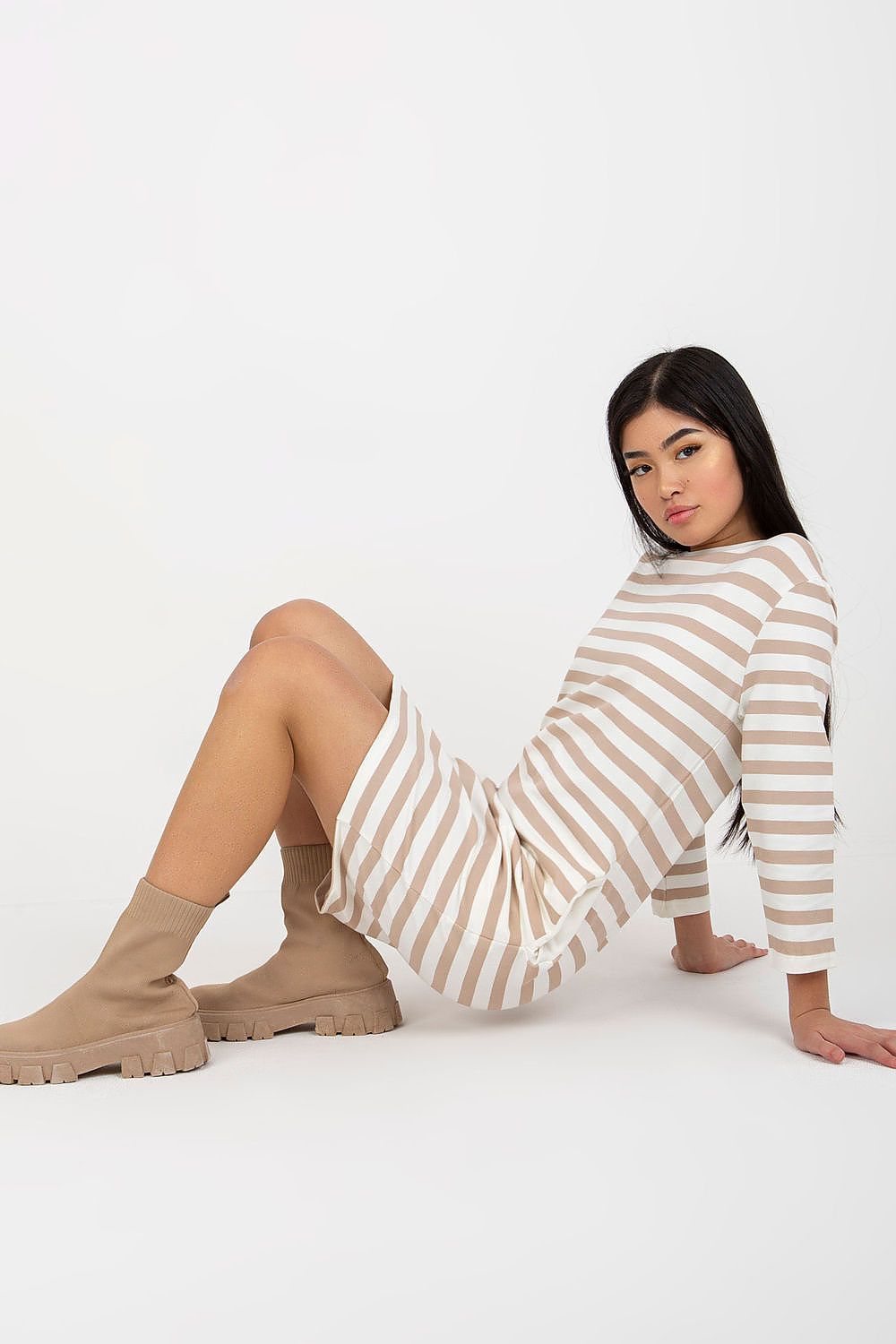 Luxuriously designed striped cotton dress with long sleeves, model seated casually showcasing the side pockets, ideal for a stylish yet comfortable look.