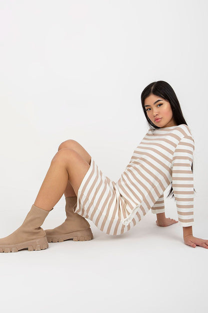 Luxuriously designed striped cotton dress with long sleeves, model seated casually showcasing the side pockets, ideal for a stylish yet comfortable look.