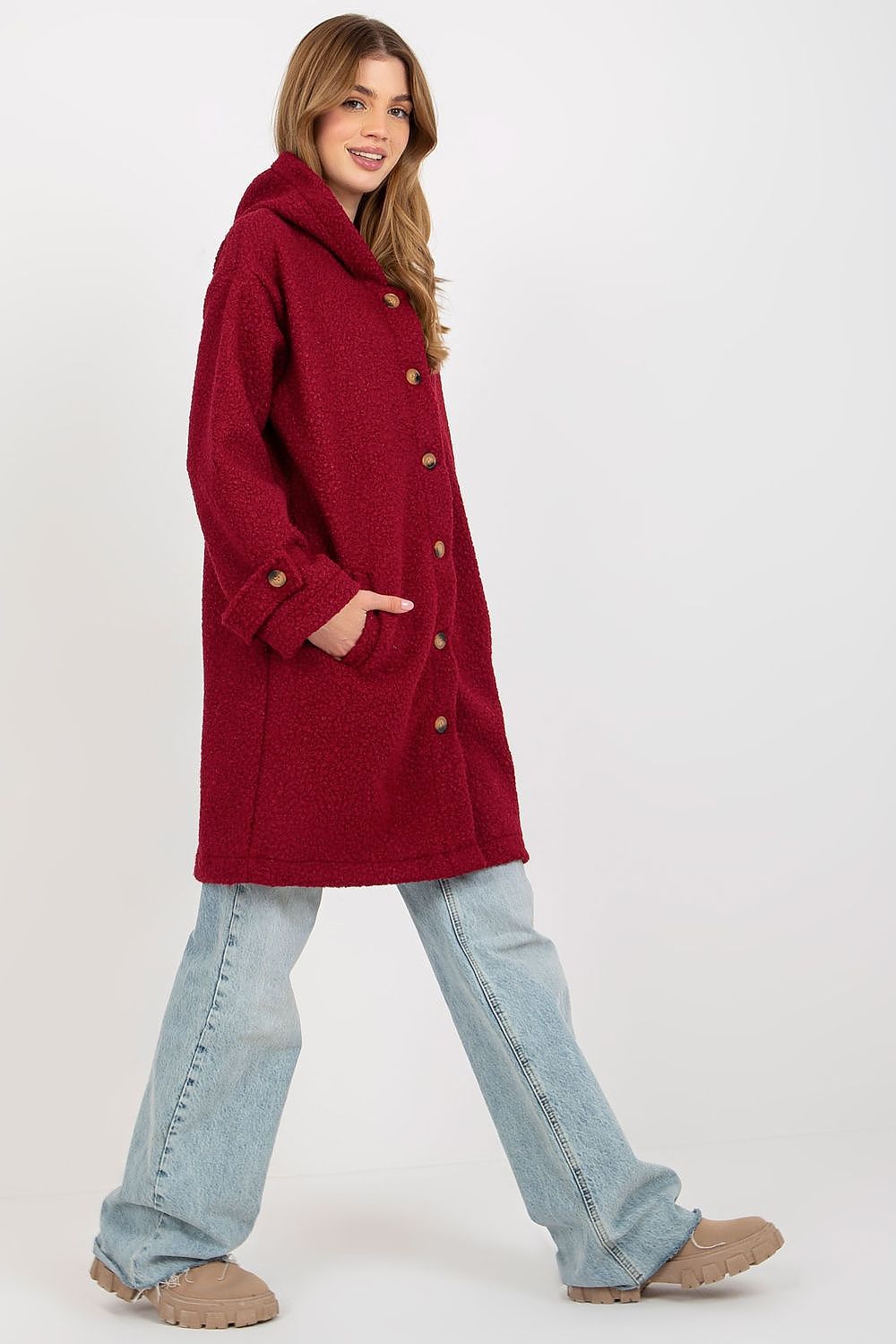 Side view of a woman in a stylish red plush coat with a button closure and hood, featuring an unlined design, complemented by relaxed denim, exuding a luxurious vibe.