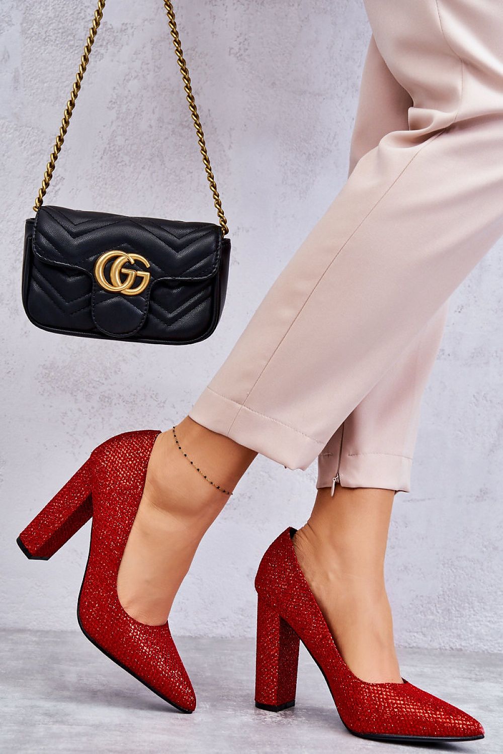 Chic red block heel pumps with an eye-catching glossy weave, elegantly paired with beige tailored trousers and a luxurious black designer handbag, embodying upscale fashion.