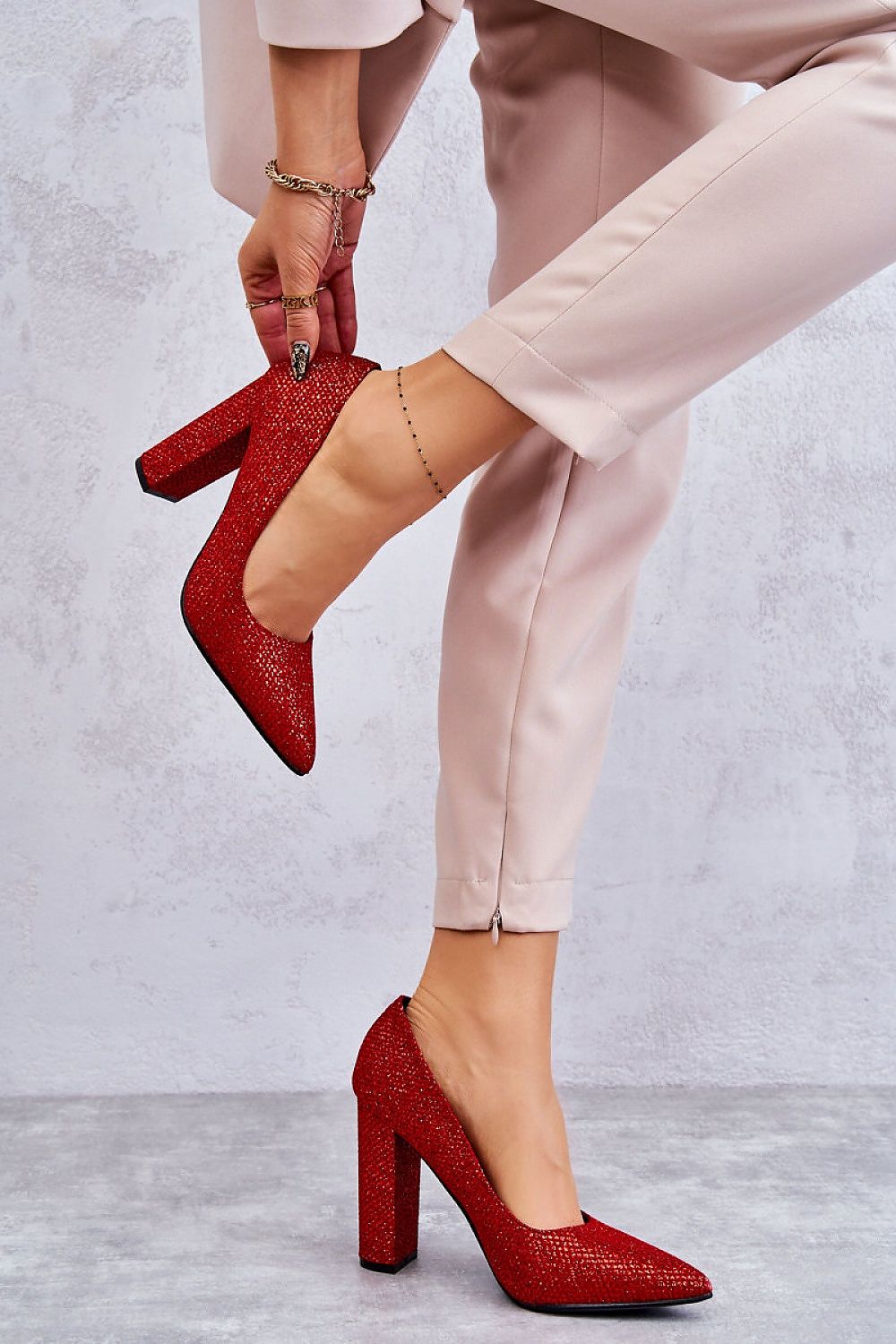Stunning red block heel pumps featuring a glossy weave design, elegantly styled on a woman's foot, paired with tailored beige trousers, perfect for a chic and sophisticated look.