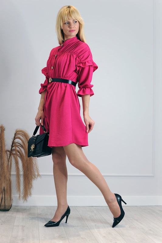 Luxurious Merribel Daydress in vibrant pink, featuring elegant frills and a loose cut, styled with a black belt and paired with chic black heels, showcasing modern femininity in an upscale setting.