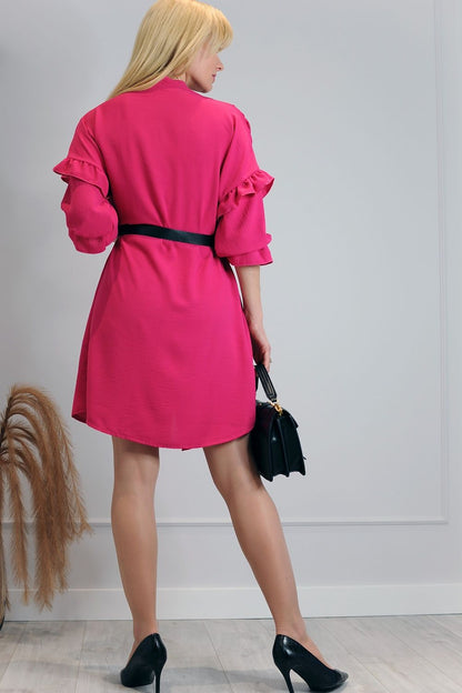 Elegant Merribel Daydress in vibrant pink, featuring feminine frills and a chic loose cut, styled with a black belt and paired with heeled shoes, showcasing a luxurious design in a stylish indoor setting.